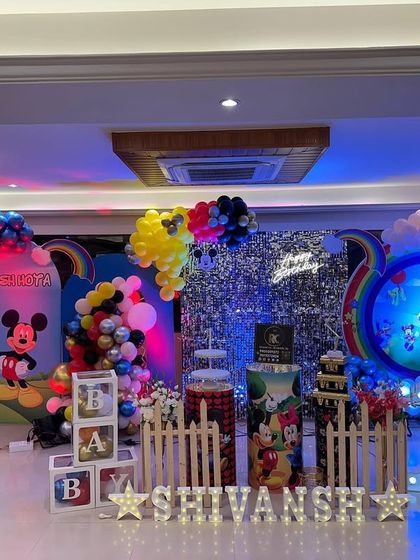 A classic Mickey Mouse Clubhouse theme with a rainbow and shimmer wall backdrop. The setup includes character cutouts, 'BABY' blocks, and a light-up number '1'.