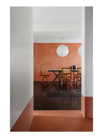 A glimpse into a dining room featuring a long table with a marble top and a black metal base. I enjoy contrasting materials to create visual interest, pairing the cool stone with the warm, textured wall.