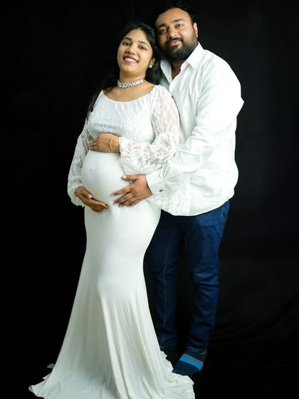 A classic and elegant couple portrait. The mom-to-be wears a beautiful white lace gown while her partner stands with her, both sharing a happy moment. This was shot against a simple black backdrop to make them stand out.