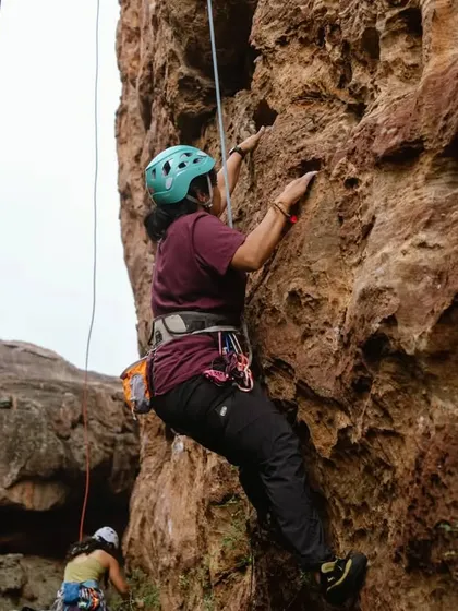 A climber on a top-rope setup, with her belayer managing the rope below. This is a safe and encouraging way for beginners to experience the height and movement of roped climbing.