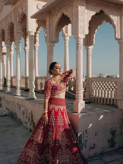 The bride strikes a graceful pose on the palace terrace, her red lehenga standing out against the neutral tones of the architecture.