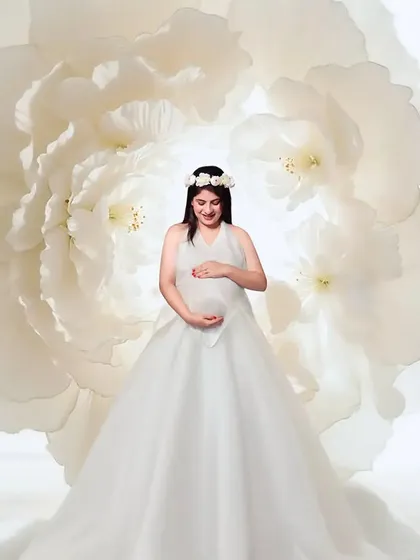 An angelic vision in white. This portrait features a beautiful white gown with a floral headpiece, set against a giant white flower prop to create a soft, ethereal, and heavenly atmosphere.