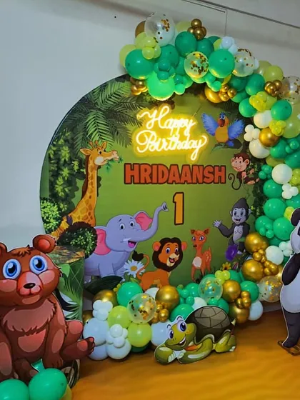 A wild Jungle theme for a first birthday! This cute setup features a backdrop with friendly cartoon animals, balloon garlands in green and gold, and adorable bear and panda cutouts.