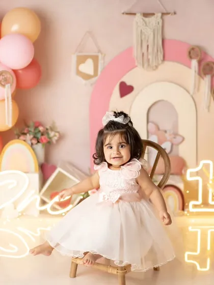 A pretty princess in a beautiful dress, sitting on a tiny chair in her colorful first birthday setup.