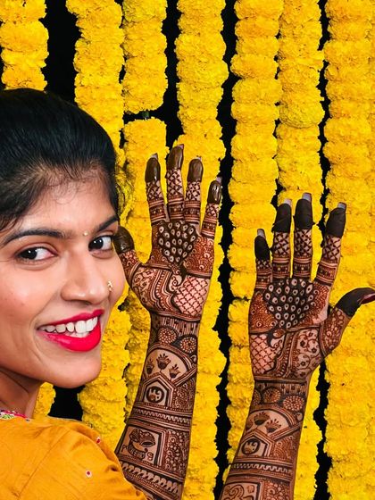 The beautiful bride Sahana, with a smile as bright as her yellow outfit and the marigold backdrop, peeking over her freshly done peacock mehendi.