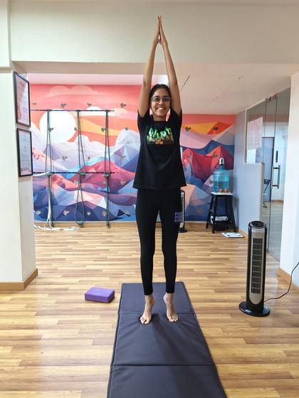 A student smiles as she holds her balance in Tadasana on tiptoes. This pose teaches focus and body awareness, with the colorful studio mural adding a touch of inspiration.