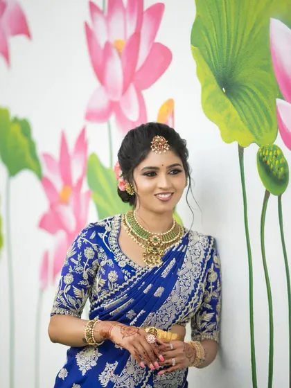 A duplicate of image 110, showing the bride in her royal blue saree against a floral backdrop.