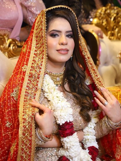 A beautiful bride with a soft, glowing makeup look. The focus is on flawless skin and defined eyes, perfect for her elegant gold and red outfit.