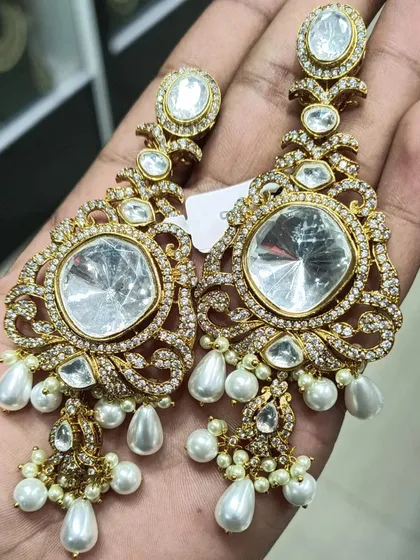 A truly statement pair of earrings for when you want to stand out. These oversized chandbalis feature large polki-style stones surrounded by American diamonds and finished with pearl drops for a very rich and glamorous look.