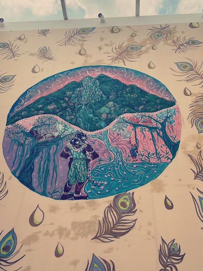 The "Kurinji" panel installed on the wall, viewed from below. The surrounding peacock feathers and water drop motifs are part of the overall design, framing the central narrative.