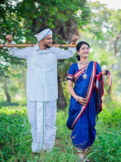A full-length shot showing the complete traditional Shetkari attire. The man carries a bamboo stick across his shoulders, adding to the authentic farmer look of the pre-wedding session.