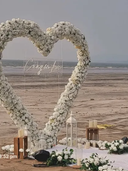 For a breathtaking beach proposal, I designed this large heart-shaped arch of white flowers right on the sand, complete with lanterns and a clear acrylic sign for a personal message.