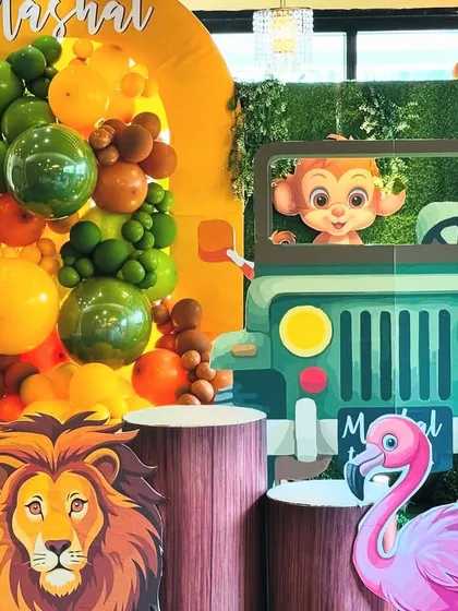 A close-up of the safari jeep prop, where a cute monkey character peeks out, ready for a photo opportunity. The scene is detailed with a lush green foliage backdrop and a vibrant balloon arrangement, highlighting the fun and interactive elements of our jungle theme.