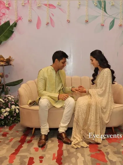 A happy couple sharing a moment during their ring ceremony. They are seated in front of our custom-designed pastel backdrop, which features delicate floral illustrations and hanging flower strings.