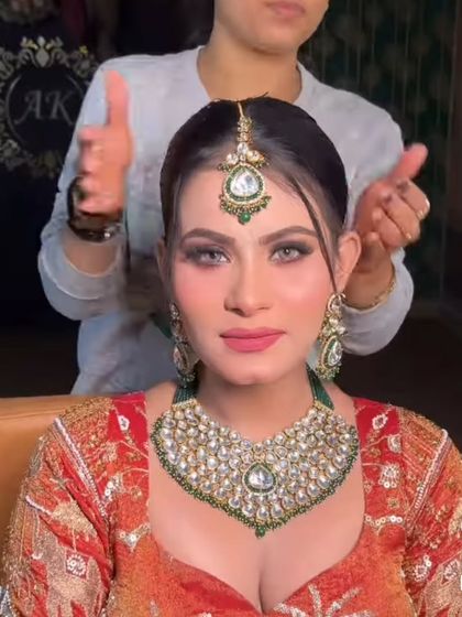 A bride getting her final touches while wearing a green and white Kundan set. The heart-shaped necklace is a modern design, perfect for a contemporary bride.