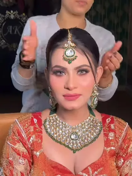 A bride getting her final touches while wearing a green and white Kundan set. The heart-shaped necklace is a modern design, perfect for a contemporary bride.