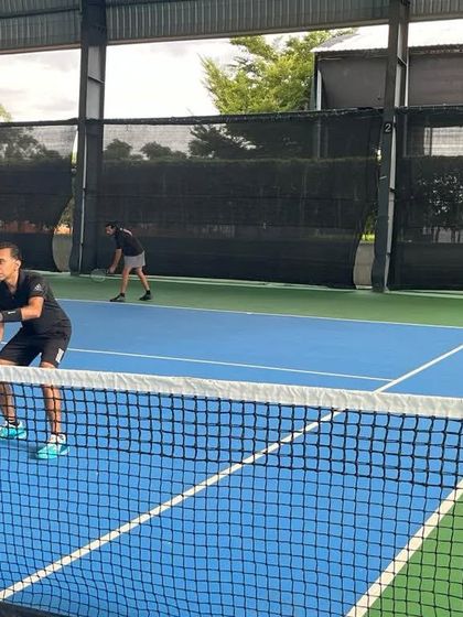 A player at the net, ready to intercept a shot in a doubles match. We welcome players who are looking to enjoy competitive tennis in a friendly environment.