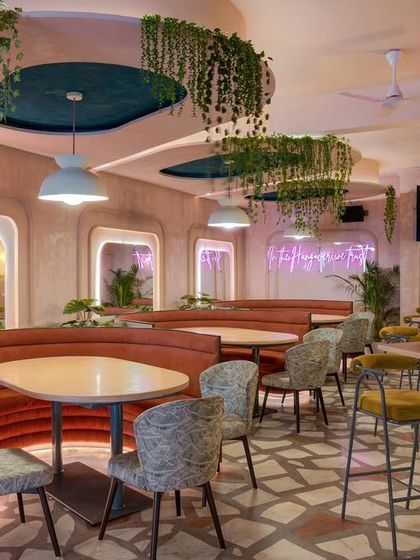 This shot highlights the custom booth seating and mirrored walls at Hangover. The mirrors amplify the sense of space, while the neon signage and hanging greenery add to the playful atmosphere.