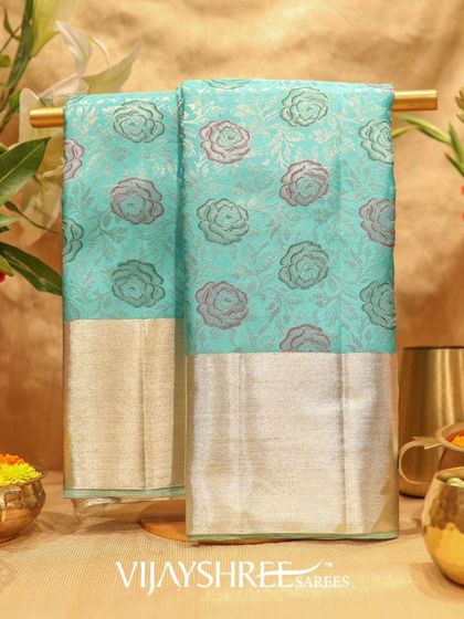 A refreshing floral Kanjivaram in aqua blue with a silver zari border. The body is adorned with woven rose motifs in shades of pink and grey.