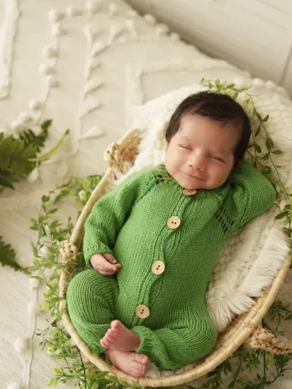 A happy, smiling newborn in a green knit outfit, nestled in a woven basket. We aim to capture a range of expressions, from sleepy to smiley.