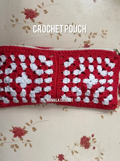 A closer look at our red and white granny square pouch, featuring a delicate flower charm on the zipper. It's a timeless design that combines traditional craft with everyday function.