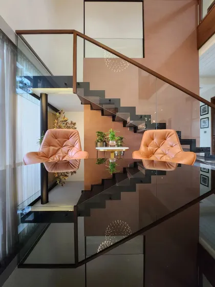 A unique perspective of a floating staircase with glass railings, reflecting the leather armchairs and creating an interesting visual illusion. The design emphasizes clean lines and the interplay of different materials like glass, metal, and wood.