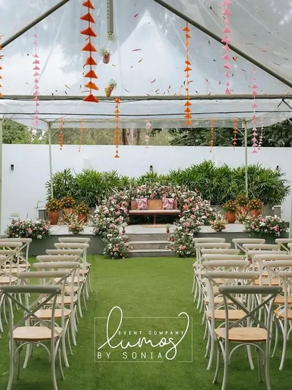 An ethnic-inspired baby shower setup under a clear tent. The stage is adorned with beautiful floral arrangements, creating a bright and celebratory space for the parents-to-be.