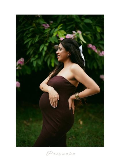 A beautiful outdoor portrait of a mother-to-be in a garden setting, surrounded by lush greenery.