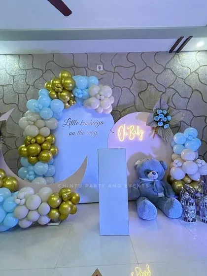 I create elegant and modern setups for baby showers, like this moon-and-stars theme. This arrangement features custom-shaped backdrops, an 'O Baby' neon sign, a giant teddy bear prop, and coordinated balloon decor in a soft blue, gold, and white palette.