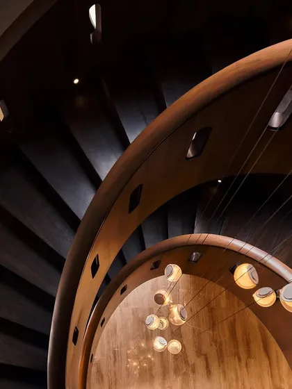 A dynamic shot looking down the spiral staircase, capturing the movement and rhythm of the wooden steps and the warm glow of the pendant lights.
