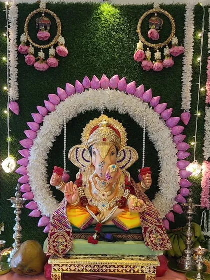 Inspired by the sacred lotus, this Ganpati decor features a central floral ring of jasmine and lotus petals against a green grass wall. The hanging floral tassels add a touch of traditional elegance to this unique design.