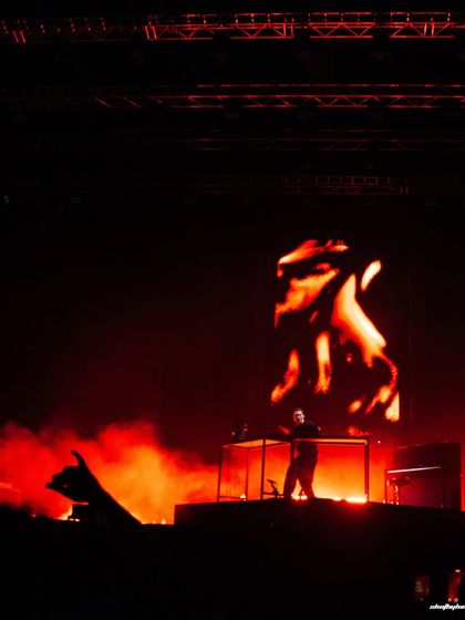 A wide, atmospheric shot of Ben Böhmer on stage, silhouetted against a fiery visual display. The image captures the scale of his solo performance.