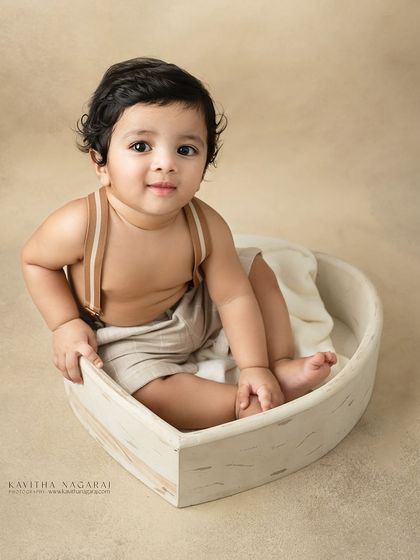 Ten-month-old twin brothers sitting in a heart-shaped basket. Their happy expressions and coordinated outfits make for an incredibly sweet portrait.