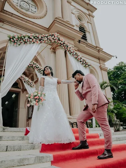 A classic, fairytale moment from a Christian wedding, with the groom kissing the bride's hand on the red-carpeted steps of the church.