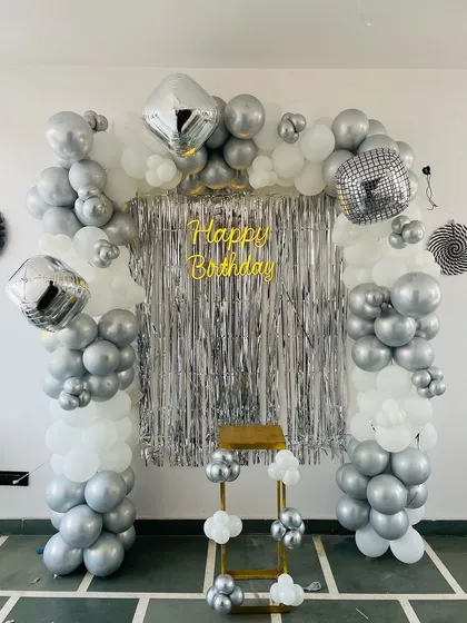 A silver and white balloon arch with a shimmer curtain and disco ball accents. This setup is perfect for a disco-themed or modern chic birthday party.