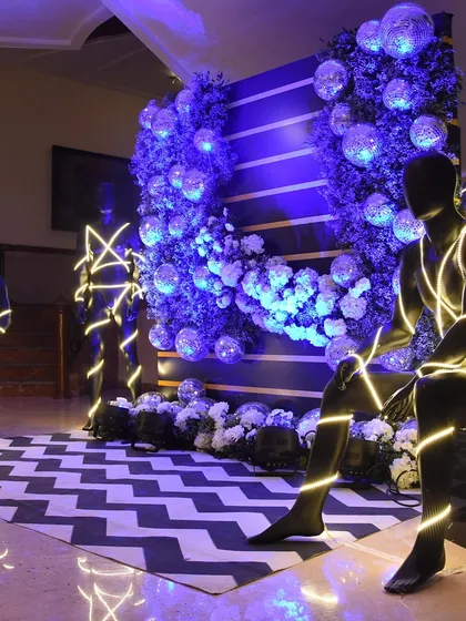 An artistic and modern photo installation with mannequins wrapped in neon lights, set against a wall of greenery and disco balls.