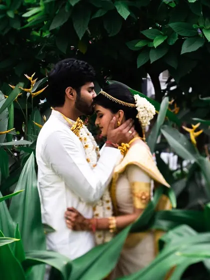 A tender forehead kiss amidst lush greenery. This intimate moment from a South Indian wedding is both romantic and serene.