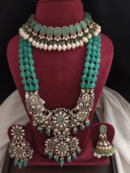 This grand bridal set in emerald green features a choker with pearl drops and a stunning layered necklace with intricate floral and peacock designs. It's a true showstopper.
