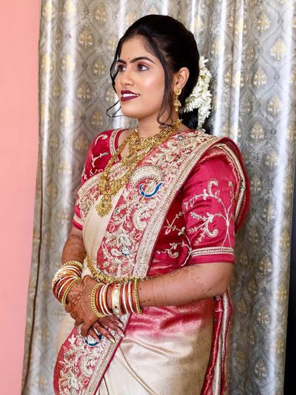 A simple and elegant look for a bride in a cream and red saree. The makeup is soft and natural, with a classic hair updo adorned with fresh flowers.