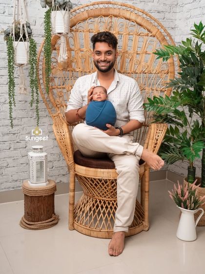 A proud father sits with his newborn son in our popular peacock chair. This setup provides a stylish and relaxed atmosphere for capturing beautiful parent and baby portraits.