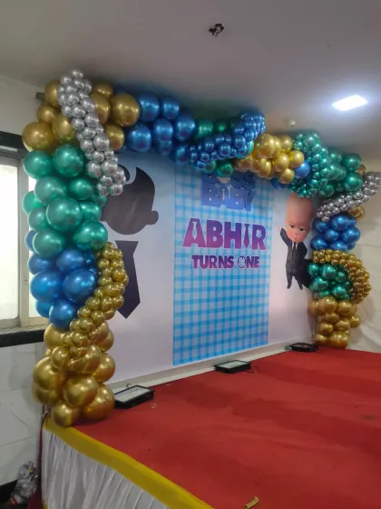 A Boss Baby themed stage backdrop for a first birthday, featuring a custom printed banner and a balloon arch in theme colors.