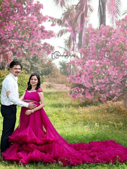 A fairytale-like portrait of a couple in a pink-themed outdoor setting. The long, flowing ruffled gown is the centerpiece of this magical shot.