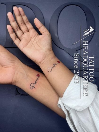 A matching couple's tattoo, with the names "Poorni" and "Chathu" inked on their respective wrists, each adorned with a small red heart.