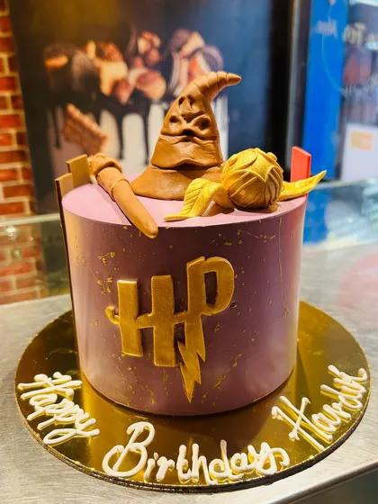 A minimalist Harry Potter cake with the iconic HP logo, a sorting hat, and a golden snitch.