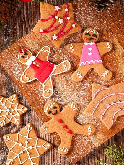 A flatlay of decorated gingerbread cookies on a wooden board, dusted with powdered sugar "snow." The warm, rustic styling creates a cozy and nostalgic Christmas feeling.