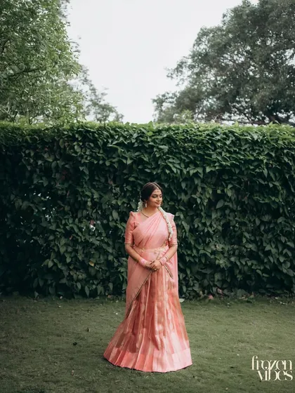 A full-length portrait of Dhriti in her elegant pink lehenga-saree, set against a wall of lush green ivy. The simplicity of the background makes her outfit stand out.