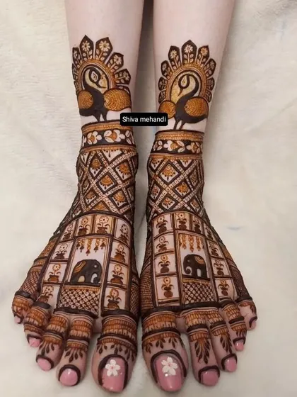 Intricate mehendi on the feet, featuring a grid of elephant motifs on the top and graceful peacocks at the ankles.