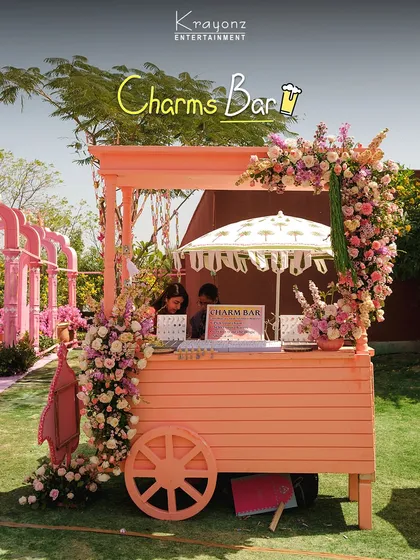 A beautiful charms bar set up in a floral-adorned cart. Guests can create their own personalized bracelets, taking home a unique and meaningful keepsake from the wedding.