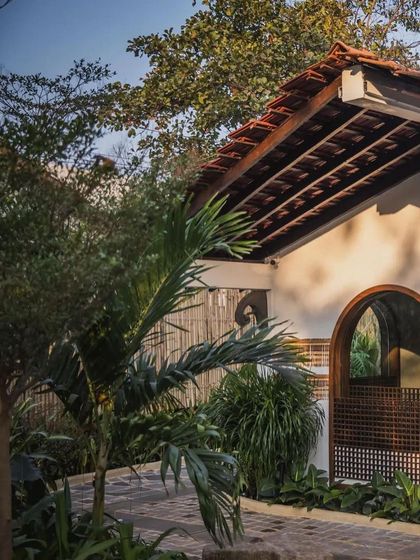 The terracotta-tiled roof and arched window of the Sanctuary Bar, surrounded by palm trees and other tropical foliage. The design captures a classic Goan architectural feel.