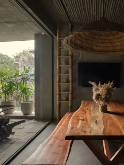 This dining area in my studio connects directly to an outdoor patio, blending rustic and modern aesthetics. The live-edge wooden table, bamboo ceiling, and raw concrete walls are all part of my philosophy of using natural, earthy materials to create spaces that feel grounded and authentic.